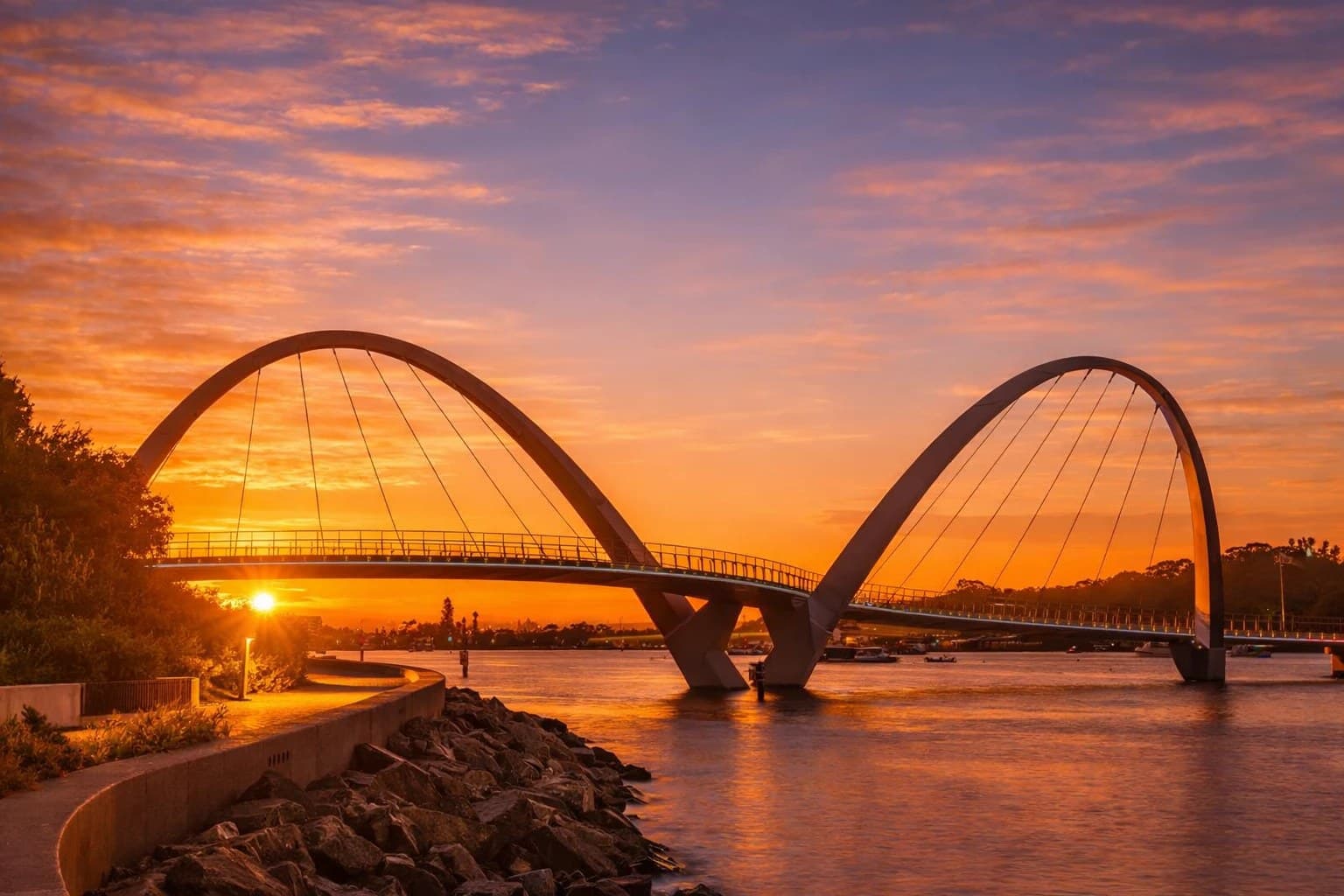 Twin-arched pedestrian bridge silhouetted against a golden sunset